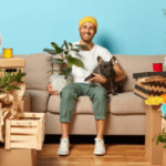 un uomo sul divano con una pianta e il suo cane e tutti gli scatoloni intorno