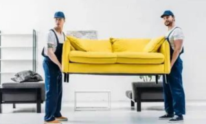 2 operai in divisa addetti allo sgombero portano un divano giallo via dal salone di un'abitazione