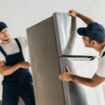 due facchini in divisa bianca e blu portano via un frigorifero