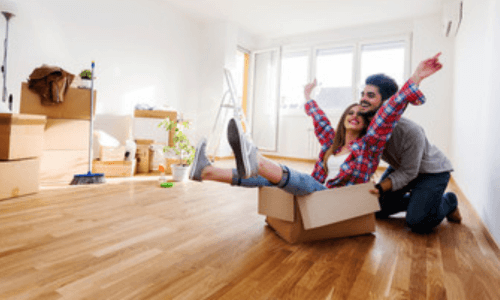 un uomo spinge una donna che è seduta in uno scatolone da trasloco in un soggiorno con parquet